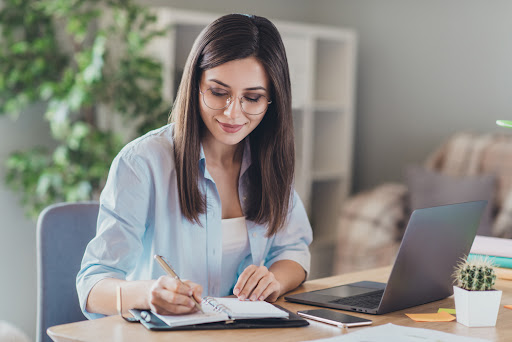 A woman sitting at a table and writing in a notebook.