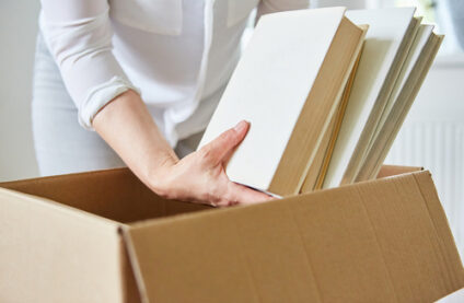 A woman places hardcover books into a cardboard box.