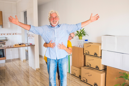 An elderly couple hugging, with moving boxes nearby.