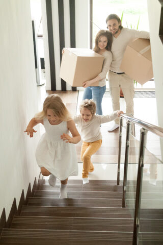 Happy children going upstairs, family with boxes moving in house