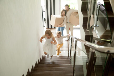 Happy children going upstairs, family with boxes moving in house
