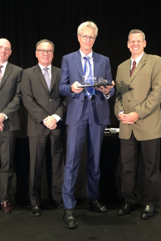 Four people in suits displaying an award.