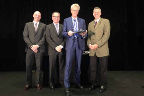 Four people in suits displaying an award.