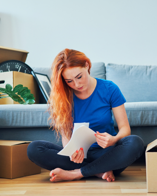 Women sitting by moving boxes reading paper