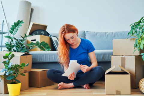 Women sitting by moving boxes reading paper