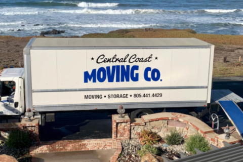 A Central coast moving company truck parked in front of a house, with crashing waves behind it.