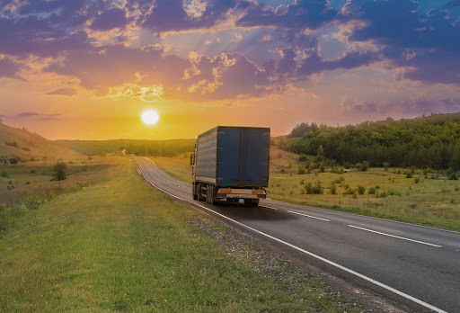 Truck moves along a suburban highway at sunset in summer.