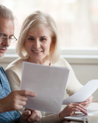 Two older people are looking at a computer and studying papers and discussing a decision.