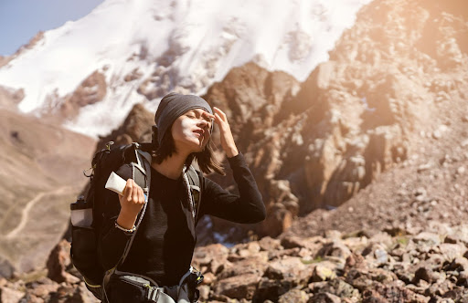 Woman hiking in elevation and applying sunscreen to her face.