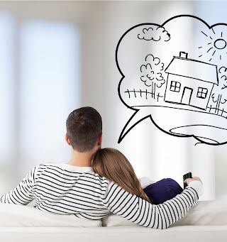 Couple sits closely together on a white couch while dreaming about moving.