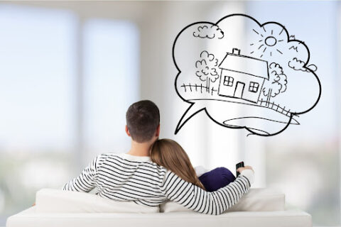 Couple sits closely together on a white couch while dreaming about moving.