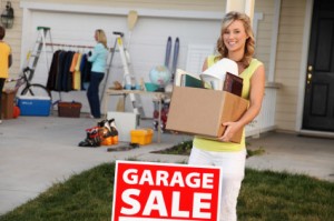 women holding a box of things behind a garage sale sign