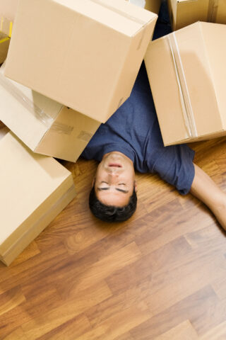 High angle view of young man sleeping underneath moving boxes