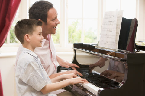 Man and young boy playing piano and smiling