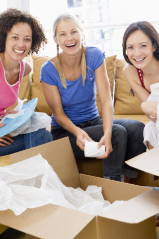 Three girl friends unpacking boxes in new home smiling