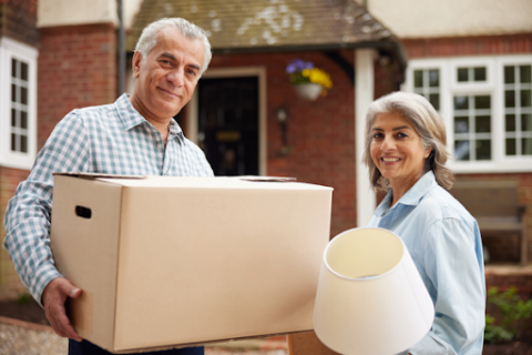 Couple standing outside of new home with cardboard box.