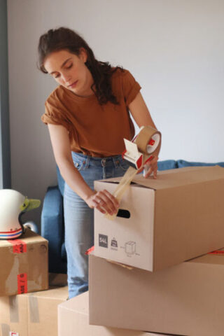 A person packing up their belongings and taping the boxes shut.