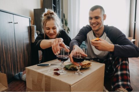 Couple unpacking and eating on a cardboard box after moving