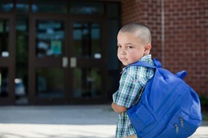 little boy wearing a blue backpack about to walk into school