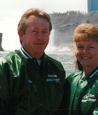 Two people smiling at the camera with a waterfall behind them.