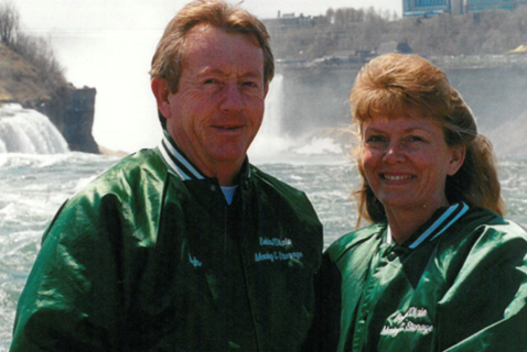 Two people smiling at the camera with a waterfall behind them.