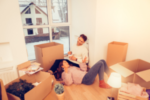 Couple on floor in new home surrounded by moving boxes.
