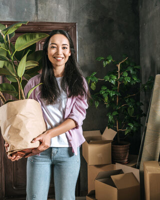 young woman with ficus plant and boxes moving into new house