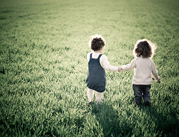 Two children hold hands and play in the grass.