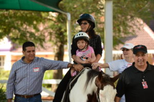 Little girl rides horse with the help of adults.