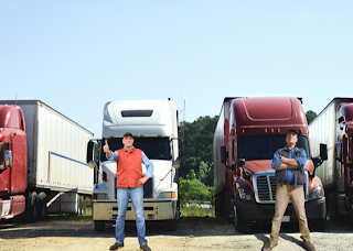 Four truck drivers posing in front of semi trucks.