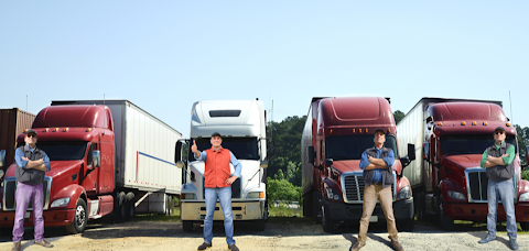 Four truck drivers posing in front of semi trucks.