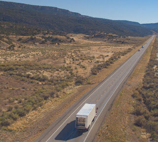 Semi truck driving down a long highway in the desert.