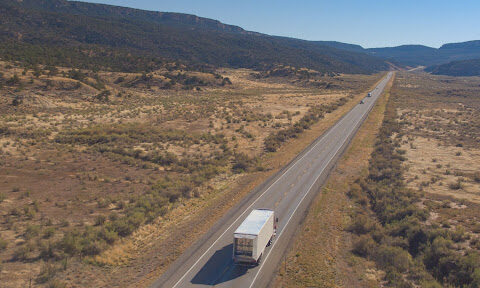 Semi truck driving down a long highway in the desert.