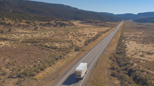 Semi truck driving down a long highway in the desert.