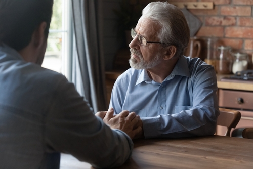 Elderly man looking upset and gazing out the window.