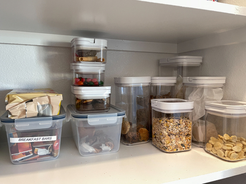 Food neatly stored in clear containers in a cabinet.