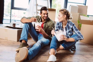 a young couple eating take out on the floor of their new home