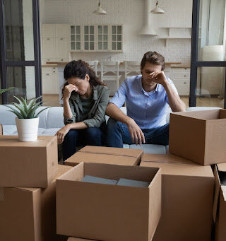 A couple sitting on the couch with their heads in their hands, looking upset.