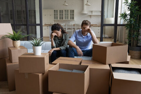 A couple sitting on the couch with their heads in their hands, looking upset.