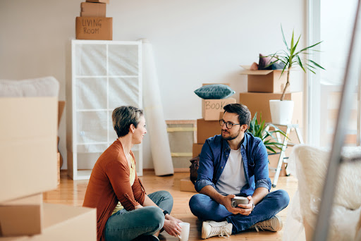 A couple sitting on the floor surrounded by boxes, engaged in conversation.