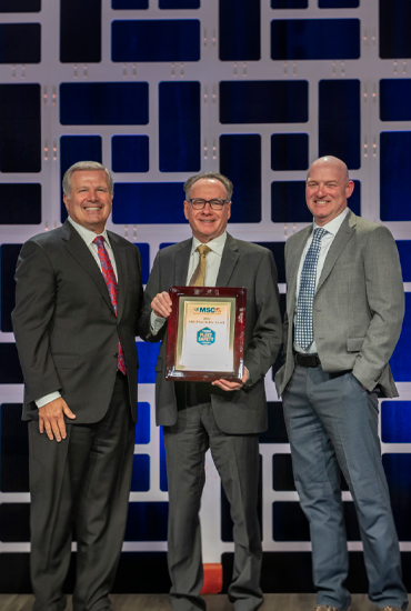 Three men in suits holding an award.