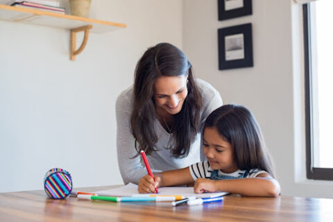 A mother and her child coloring at a table.