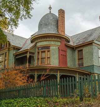 Green historic home surrounded by fence.