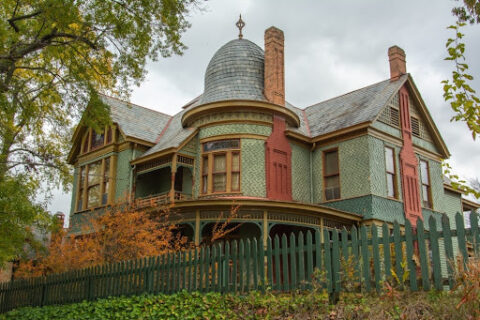 Green historic home surrounded by fence.