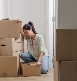 A woman looks tired and frustrated as her head leans against her arm and she kneels among her moving boxes.