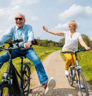 An older couple smiles while riding bikes