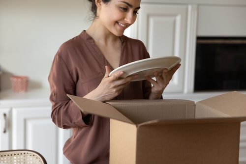 A woman smiles as she packs plates into a cardboard box.
