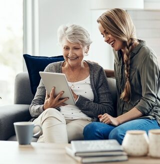 A young woman helps her grandmother with her smart tablet device.