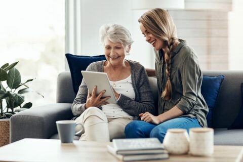 A young woman helps her grandmother with her smart tablet device.