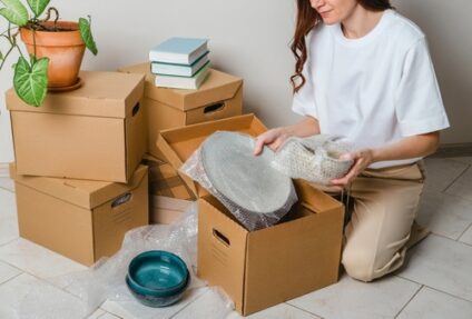 A woman packs plates, bowls, and other belongings into cardboard boxes with bubble wrap.